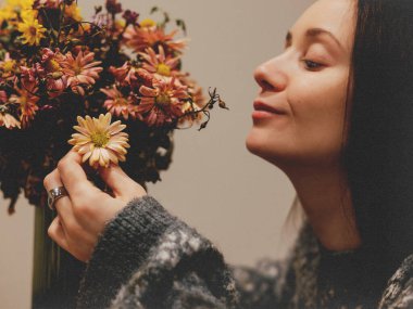 Sonbahar çiçeklerinin kokusundan hoşlanan genç bir kadın yüzünde narin bir çiçek tutuyor. Sıcak, rahat bir atmosfer sağlığa, farkındalığa, yaşam tarzına, güzelliğe odaklı hisse senetleri için mükemmel..