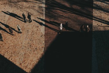 Parke taşlı bir caddede yürüyen farklı insanların soyut görüntüsü. Güçlü güneş ışığı uzun gölgeler yaratıyor. Sosyete harekete geçti. Kentsel alanda ve hareketlerde gezinen bireylerin yüksek açılı görünümü. 