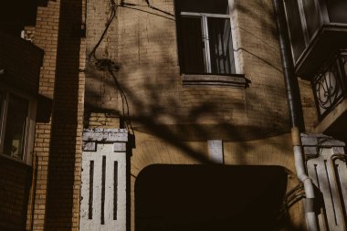 Dramatik şehir kontrastı. Karanlık kemerli eski bir Avrupa binasının dış cephesinde güneş ışığı ve derin gölgeler. Gündüz vakti soyut, kasvetli, estetik bir tarihi ev yaratıyor.