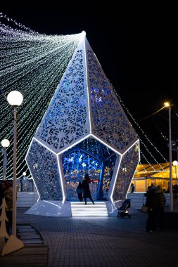 KYIV, Ukrayna 2 Aralık 2025 Yeni Yıl 2026, gece yeni yıl kurulumu, büyük, modern, geometrik kristal heykel mavi ışıklarla parıldıyor, festival sicim ışıkları ve bulanık insanlar.