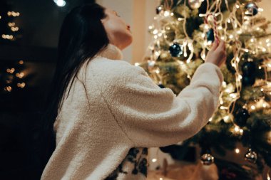 Evinde akşamları Noel ağacı süsleyen rahat, genç bir beyaz kadın. Bu sıcak, otantik yaşam tarzı çekimi kış tatili blog yazıları, pazarlama materyalleri ve şenlikli tasarımlar için mükemmel..