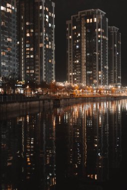 KYIV, Ukrayna 2 Aralık 2026 Night City rıhtımı modern yerleşim yerlerinin bulunduğu sakin sulara yansıyor. Şehir yaşam tarzı, şehir ışıkları, lüks yaşam, gayrimenkul konsepti, akşam manzarası.