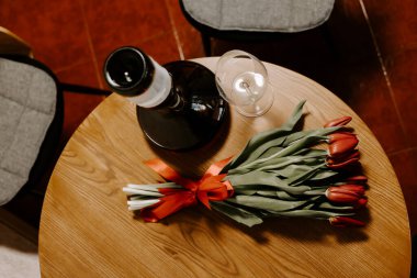 Şarap sürahisi ve camın yanında tahta bir masada kurdeleli kırmızı lale buketinin en üst görüntüsü. Yumuşak ışıklandırmalı eski moda bir hayat. Romantik ve kutlama tasarım temaları için ideal.