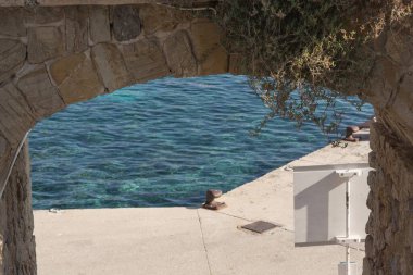 İskele duvarında paslı bir kazık, paslı bir zincir ve arka planda Akdeniz 'in limanındaki su..