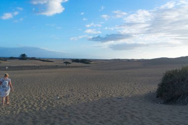 Çöldeki kum tepelerinin kumlarında yürüyen bir kadın, parlak bir yaz gününde beyaz kumda yürüyen genç bir kadın, tatil konsepti.