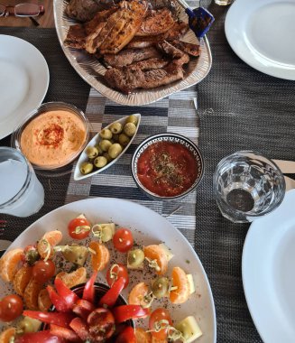 Köy ahşap masada ızgara et ve sebzelerle servis edilen peynir tabağı.