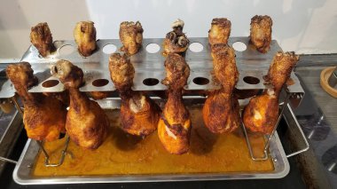 Terbiye edilmiş tavuk budu ve kanatları, damlayan tavanın üzerinde dikey olarak paslanmaz çelik bir stantta kızartılır..