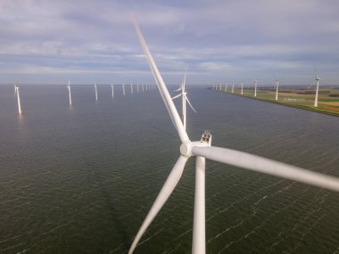 Bulutları ve mavi gökyüzü olan off-shore yel değirmeni parkı, okyanusta rüzgar türbinli drone hava manzaralı yel değirmeni.