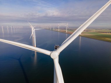 Bulutları ve mavi gökyüzü olan off-shore yel değirmeni parkı, okyanusta rüzgar türbinli drone hava manzaralı yel değirmeni.