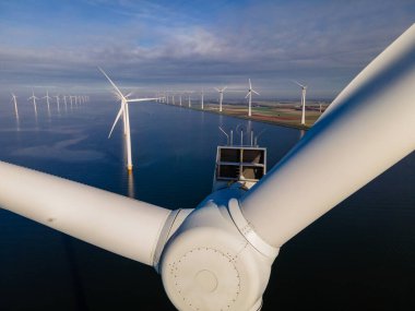 Bulutları ve mavi gökyüzü olan off-shore yel değirmeni parkı, okyanusta rüzgar türbinli drone hava manzaralı yel değirmeni.