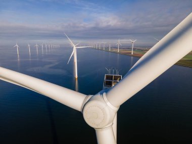 Bulutları ve mavi gökyüzü olan off-shore yel değirmeni parkı, okyanusta rüzgar türbinli drone hava manzaralı yel değirmeni.