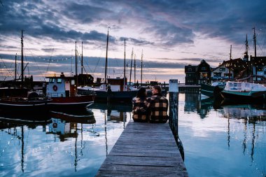 Urk Flevoland Holland, iki erkek ve kadın Urk Hollanda 'nın küçük balıkçı köyü limanında gün batımını izliyorlar.