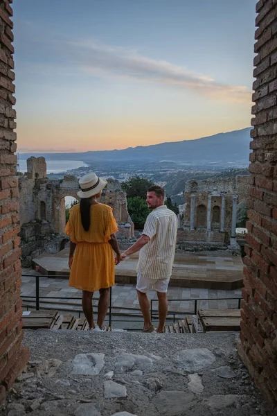 Пара мужчин и женщин посещают руины древнегреческого театра в Таормине на фоне вулкана Этна, Италия. Таормина расположена в Мессине, на восточном побережье острова Сицилия. — стоковое фото