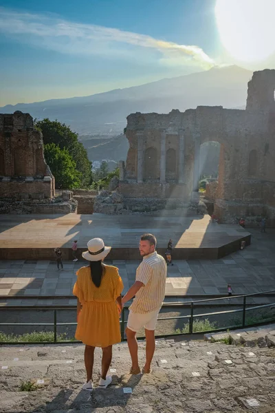Paar Männer und Frauen besuchen Ruinen des antiken griechischen Theaters in Taormina vor dem Hintergrund des Vulkans Ätna, Italien. Taormina liegt in der Metropolstadt Messina, an der Ostküste der Insel Sizilien. — Stockfoto
