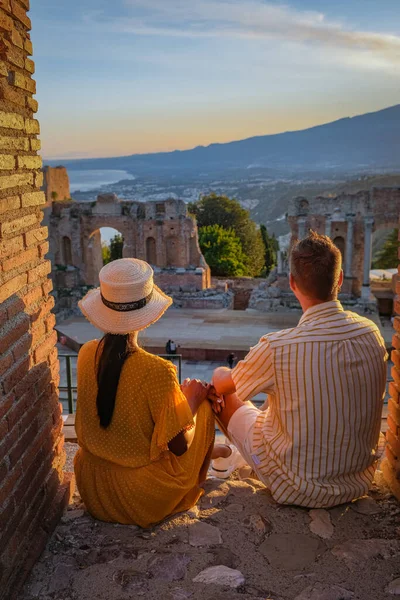 Пара мужчин и женщин посещают руины древнегреческого театра в Таормине на фоне вулкана Этна, Италия. Таормина расположена в Мессине, на восточном побережье острова Сицилия. — стоковое фото