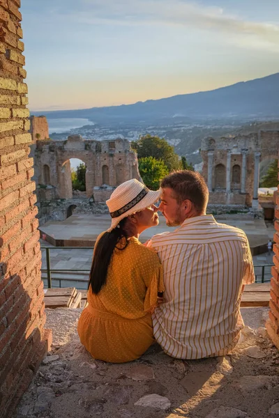Couple men and woman visit Ruins of Ancient Greek theatre in Taormina on background of Etna Volcano, Italy. Taormina located in Metropolitan City of Messina, on east coast of island of Sicily. — Stock Photo, Image