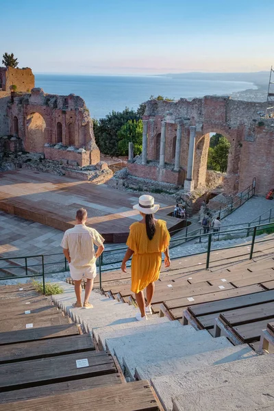 Cuplu de bărbați și femei vizitează ruinele teatrului grec antic din Taormina pe fundalul vulcanului Etna, Italia. Taormina situat în orașul metropolitan Messina, pe coasta de est a insulei Sicilia . — Fotografie, imagine de stoc