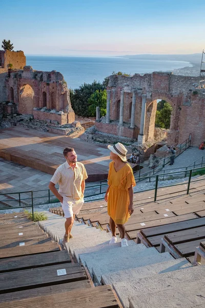 Cuplu de bărbați și femei vizitează ruinele teatrului grec antic din Taormina pe fundalul vulcanului Etna, Italia. Taormina situat în orașul metropolitan Messina, pe coasta de est a insulei Sicilia . — Fotografie, imagine de stoc