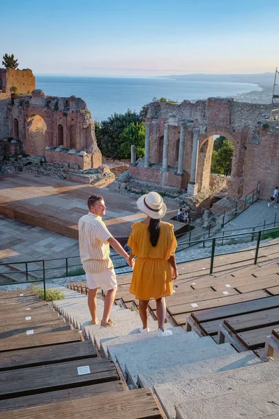 Cuplu de bărbați și femei vizitează ruinele teatrului grec antic din Taormina pe fundalul vulcanului Etna, Italia. Taormina situat în orașul metropolitan Messina, pe coasta de est a insulei Sicilia . — Fotografie, imagine de stoc