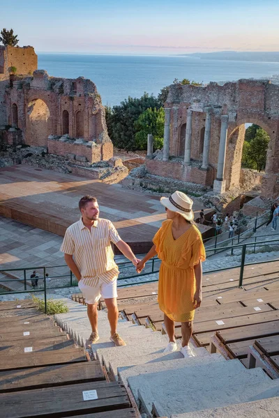 Cuplu de bărbați și femei vizitează ruinele teatrului grec antic din Taormina pe fundalul vulcanului Etna, Italia. Taormina situat în orașul metropolitan Messina, pe coasta de est a insulei Sicilia . — Fotografie, imagine de stoc