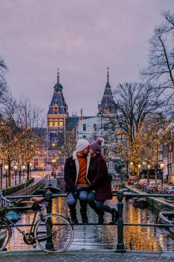 Amsterdam 'a şehir gezisine çıkan çift, Aralık ayı boyunca yılbaşı ışıklarıyla, geceleyin Amsterdam' ın kanal tarihi merkeziyle,