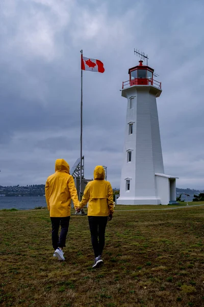 Vancouver Island, Canada, Quadra Island old historical lighthouse at Cape Mudge couple in yellow rain coat during storm by the coast