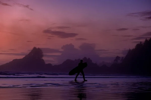 Vancouver Island Tofino, sunset at the beach with surfers in the ocean, beautiful colorful sunset with pink and purple colors in the sky at Vancouver Island with pople surfing