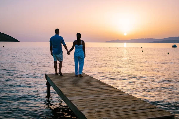Çift, ahşap bir iskelede oturmuş denizin üzerinde renkli bir gün batımını izliyordu. Girit Yunanistan 'da gün batımını izleyen erkek ve kadın. — Stok fotoğraf
