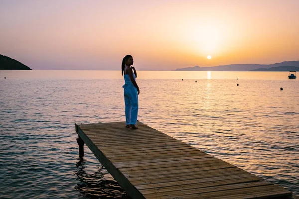 Frau steht auf einem hölzernen Steg und sieht einen bunten Sonnenuntergang über dem Meer, Männer und Frauen beobachten den Sonnenuntergang auf Kreta Griechenland — Stockfoto