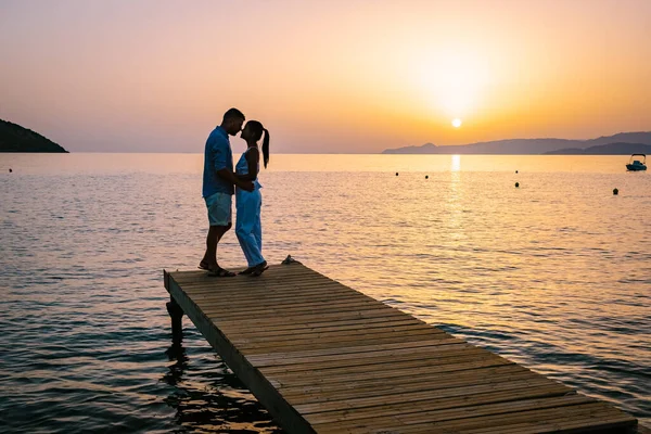 Pár ült egy fából készült mólón, látszó színes naplemente a tengeren, férfiak és nők nézi naplemente Kréta Görögország — Stock Fotó