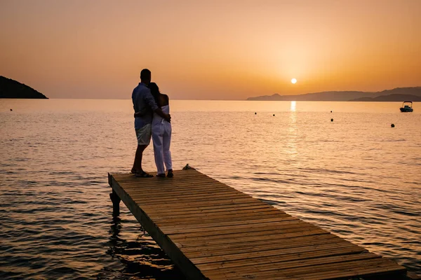 Par sitter på en träbrygga, ser en färgstark solnedgång på havet, män och kvinnor tittar på solnedgången på Kreta Grekland — Stockfoto