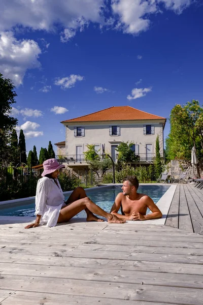 Pareja de hombres y mujeres que se relajan junto a la piscina en una villa de Francia en la Provenza, hombre y mujer en traje de baño y bañador en la piscina durante las vacaciones en Francia —  Fotos de Stock