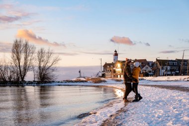 Kış boyunca Hollanda 'nın Urk deniz fenerinin yanında karlar altında birkaç erkek ve kadın.