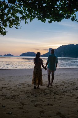 Çiftler sahilde gün batımını, Eropean erkeği ve Asyalı kadın gün batımını Krabi Tayland sahilinde seyrediyor.