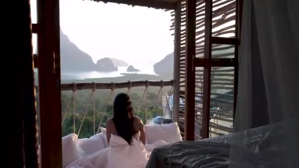 Bahía de Phangnga, mujer asiática despertando en la cama en la selva natural mirando hacia el océano y la selva durante el amanecer en la cabaña de madera en las montañas de Tailandia — Vídeo de stock