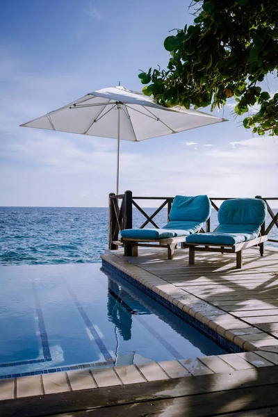 Rahatlatıcı yaz plajı, güneşlenme güvertesi ve sahilde palmiye ağaçları ve Curacao lüks evindeki panoramik deniz manzaralı özel yüzme havuzu.