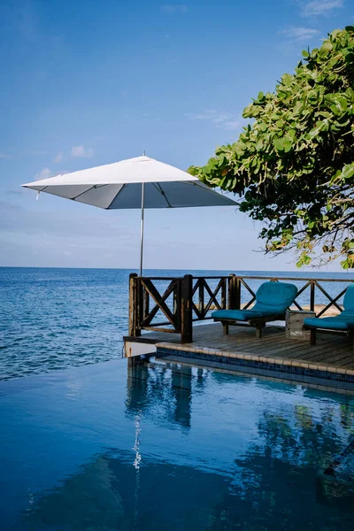 Rahatlatıcı yaz plajı, güneşlenme güvertesi ve sahilde palmiye ağaçları ve Curacao lüks evindeki panoramik deniz manzaralı özel yüzme havuzu.