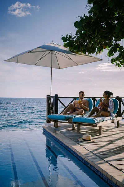 Rahatlatıcı yaz plajı, güneşlenme güvertesi ve sahilde palmiye ağaçları ve Curacao lüks evindeki panoramik deniz manzaralı özel yüzme havuzu.