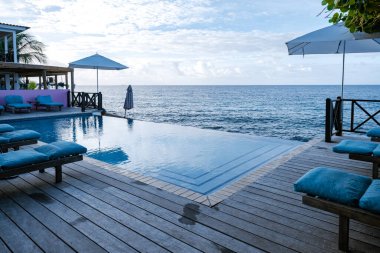 Rahatlatıcı yaz plajı, güneşlenme güvertesi ve sahilde palmiye ağaçları ve Curacao lüks evindeki panoramik deniz manzaralı özel yüzme havuzu.