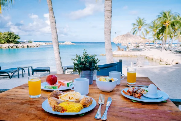 Petit déjeuner sur une table au bord de la plage avec vue sur l'océan, mer des Caraïbes avec table de petit déjeuner avec jus d'orange café et croissants et fruits — Photo