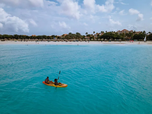 Aruba Caribbean couple men and woman mid age in kayak in blue ocean on the beach with palm trees — Stock Photo, Image
