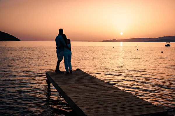 Para siedząca na drewnianym pomoście, wyglądająca na kolorowy zachód słońca nad morzem, mężczyźni i kobiety oglądający zachód słońca na Krecie Grecja — Zdjęcie stockowe