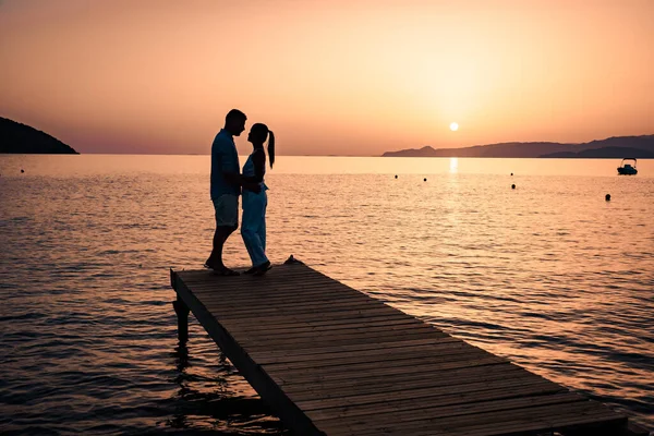 Casal sentado em um molhe de madeira, olhando um pôr do sol colorido no mar, homens e mulheres assistindo pôr do sol em Creta Grécia — Fotografia de Stock