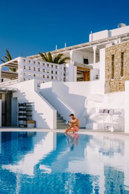 Sonsuz yüzme havuzunda dinlenen, okyanusa bakan, havuzda havuz başında kitap okuyan bir adam.