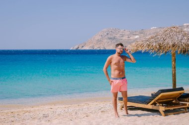 Mikonos plajında, Mikonos plajında, Mikonos plajında, Mikonos plajında, yaz boyunca şemsiyeli ve lüks plaj sandalyeli, Elia sahilinde mavi okyanus Mikonos Yunanistan 'da.
