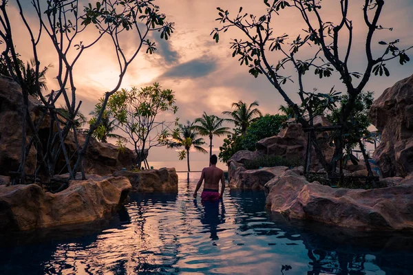 Piscina de luxo em resort tropical, férias relaxantes na Tailândia. , Jovem durante o pôr do sol pela piscina em Pattaya — Fotografia de Stock