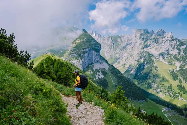 A woman with a backpack stands on top of a mountain , The girl travels to beautiful places, Reaching the goal, mountain ridge at Saxer Luecke , Kreuzberge in Alpstein Appenzell Innerrhoden Switzerland — Stock Photo, Image