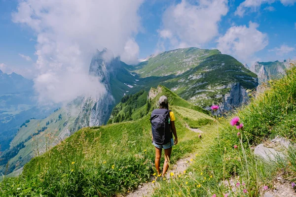 A woman with a backpack stands on top of a mountain , The girl travels to beautiful places, Reaching the goal, mountain ridge at Saxer Luecke , Kreuzberge in Alpstein Appenzell Innerrhoden Switzerland — Stock Photo, Image