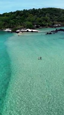 Bask in the beauty of Koh Kham Island, Thailand, where tranquil waters meet lush greenery. People enjoy a serene day under the sun, a couple of caucasian men and Asian women on vacation