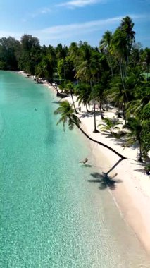 Soft white sand and lush palm trees. Guests relax under the sun, enjoying the tranquility of Koh Koods pristine beauty.A woman on a swing under a palm tree in a tropical paradise 